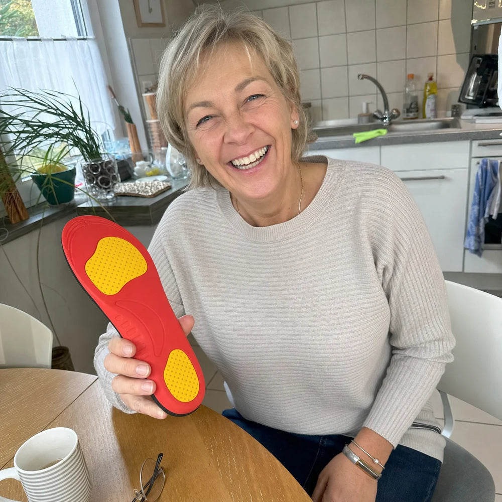 Laura lacht am Küchentisch und hält eine Ortavio ArcCore Einlegesohle
